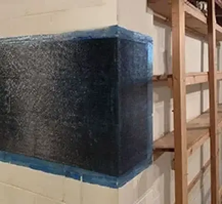 A basement wall corner reinforced with a black carbon fiber wrap, next to wooden shelves.