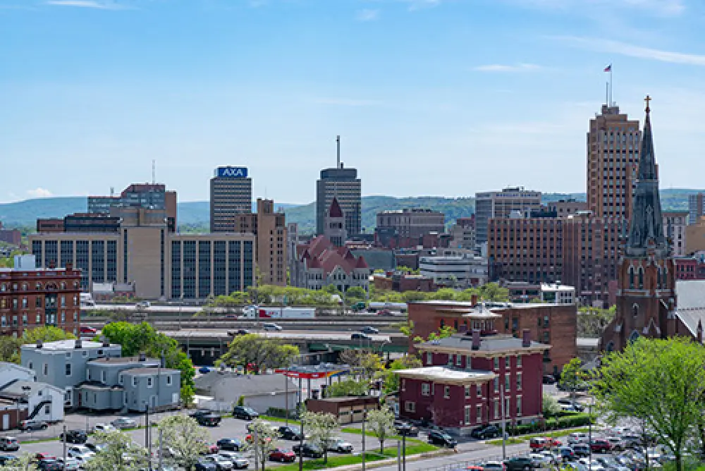View of a city skyline with tall buildings, a church, and houses under a clear blue sky.