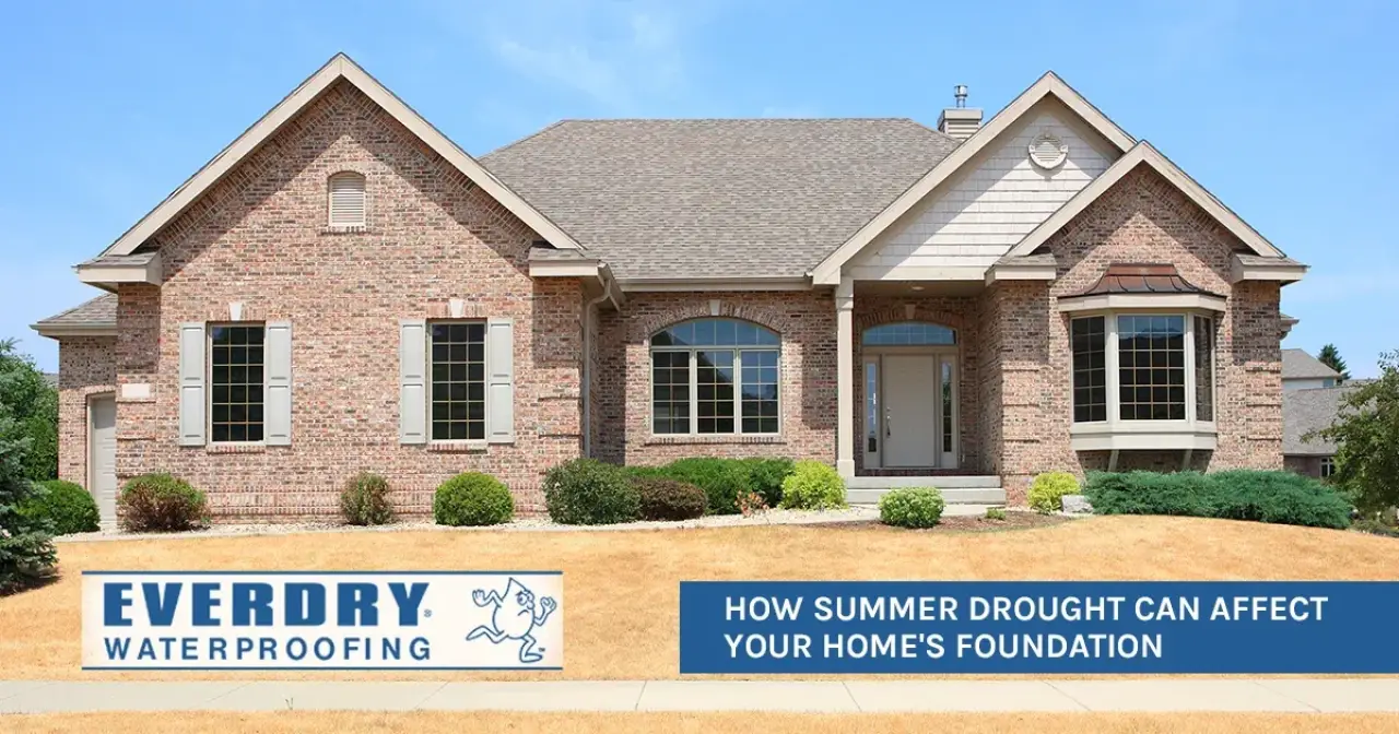 A brick house with dry, yellow grass in front and a sign about summer drought foundation risks.