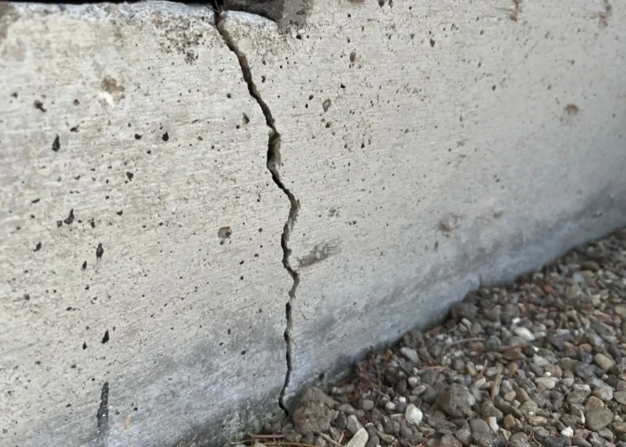 A vertical crack runs through a concrete wall above gravel.