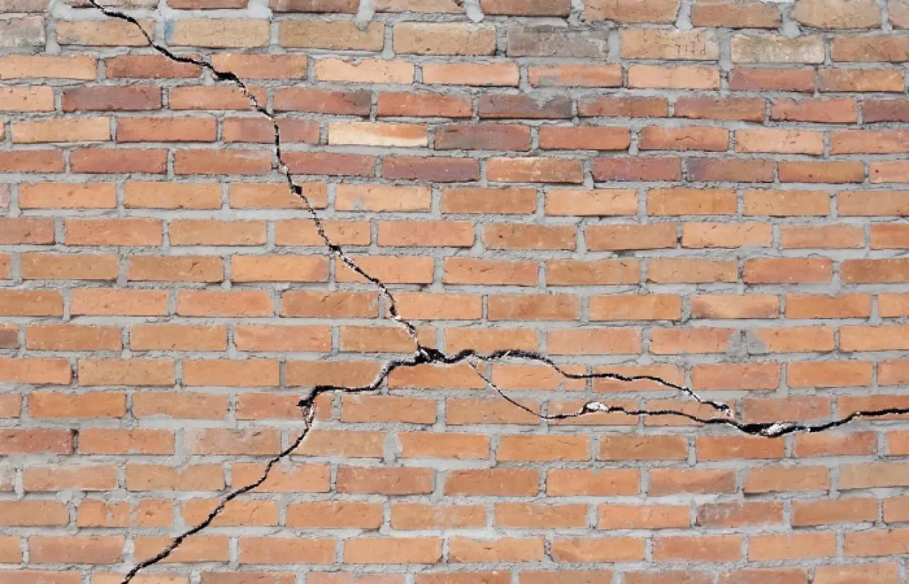 A brick wall with two large, jagged cracks running across its surface.