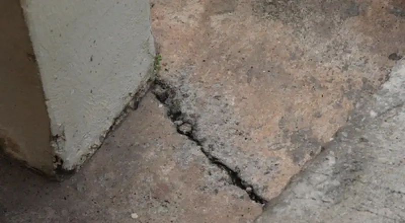 A cracked concrete floor near a wall and a sloped surface, showing signs of damage.