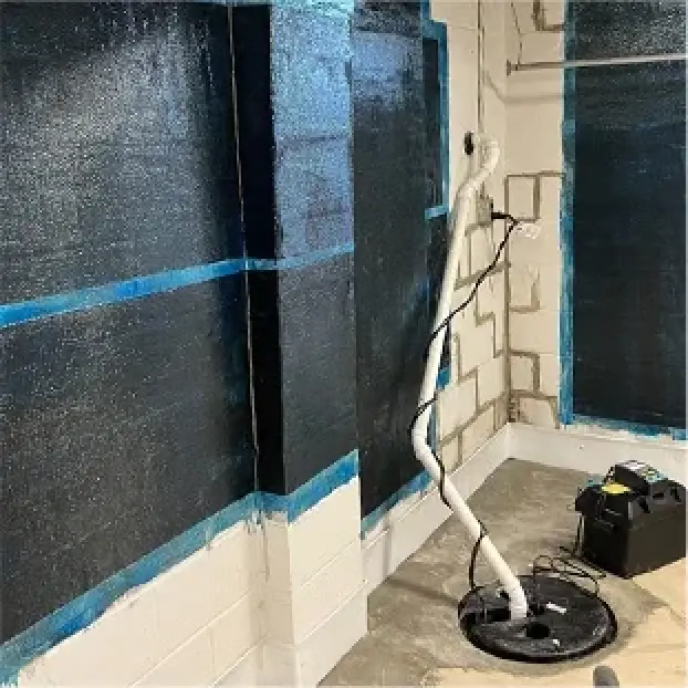 Black waterproofing on basement walls with blue tape, a white sump pump, and exposed floor.