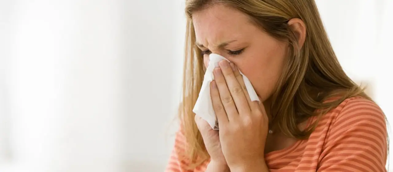 Woman wearing an orange shirt and blowing her nose into a tissue.