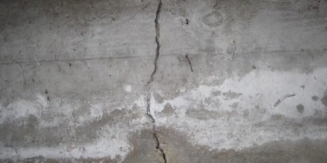 A cracked concrete wall with discoloration and visible signs of wear and damage.