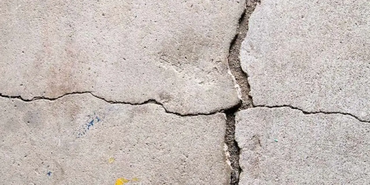 Close-up of cracked concrete with intersecting lines and small yellow and blue paint spots.
