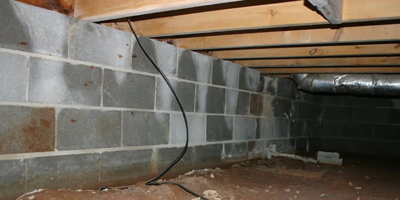 A crawl space with cinder block walls, exposed wood beams, dirt floor, and some wiring visible.