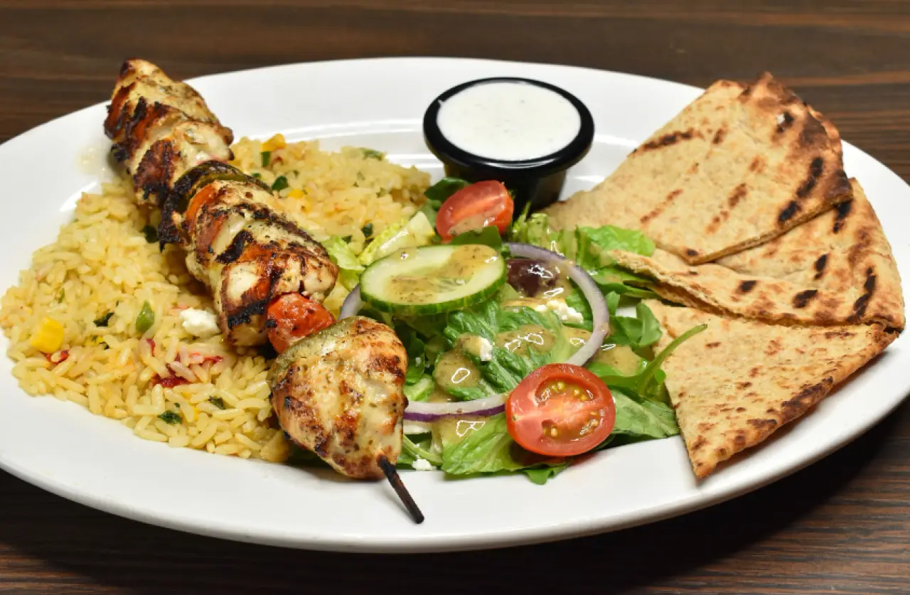 Grilled chicken skewer with rice, salad, pita, and dipping sauce.