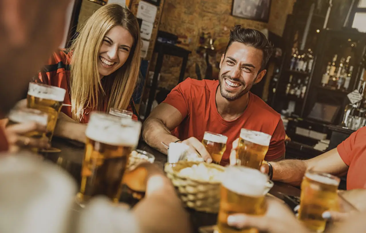 Friends laughing over beers at a restaurant table.