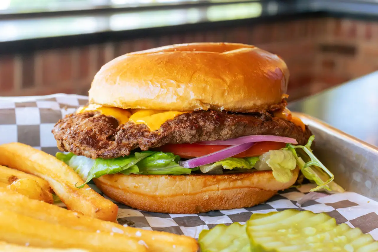 Cheeseburger with lettuce, tomato, fries, and pickle slices on a checkered tray.