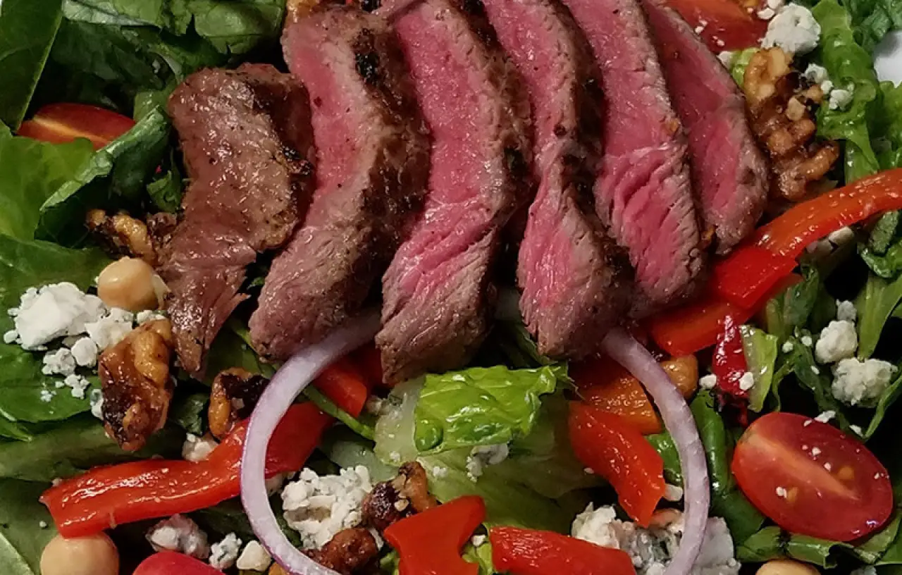 Sliced steak salad with greens, tomatoes, peppers, walnuts, and cheese.