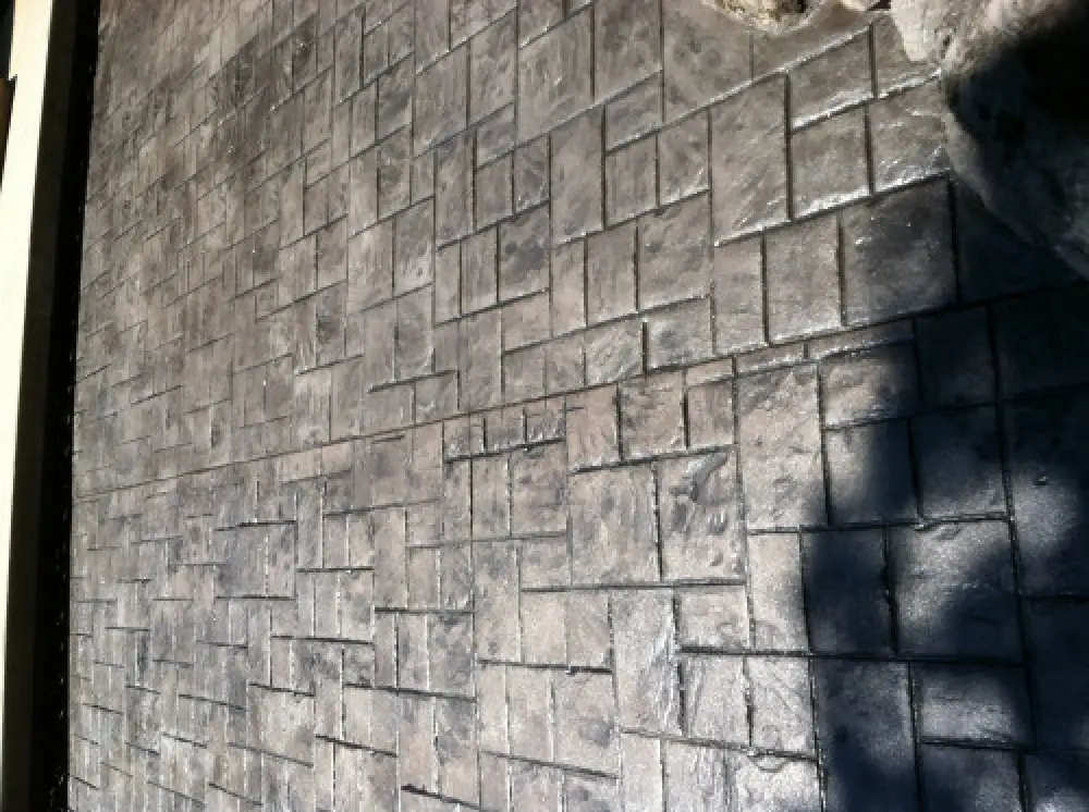 Gray stamped concrete with a rectangular and square tile pattern in sunlight and partial shadow.
