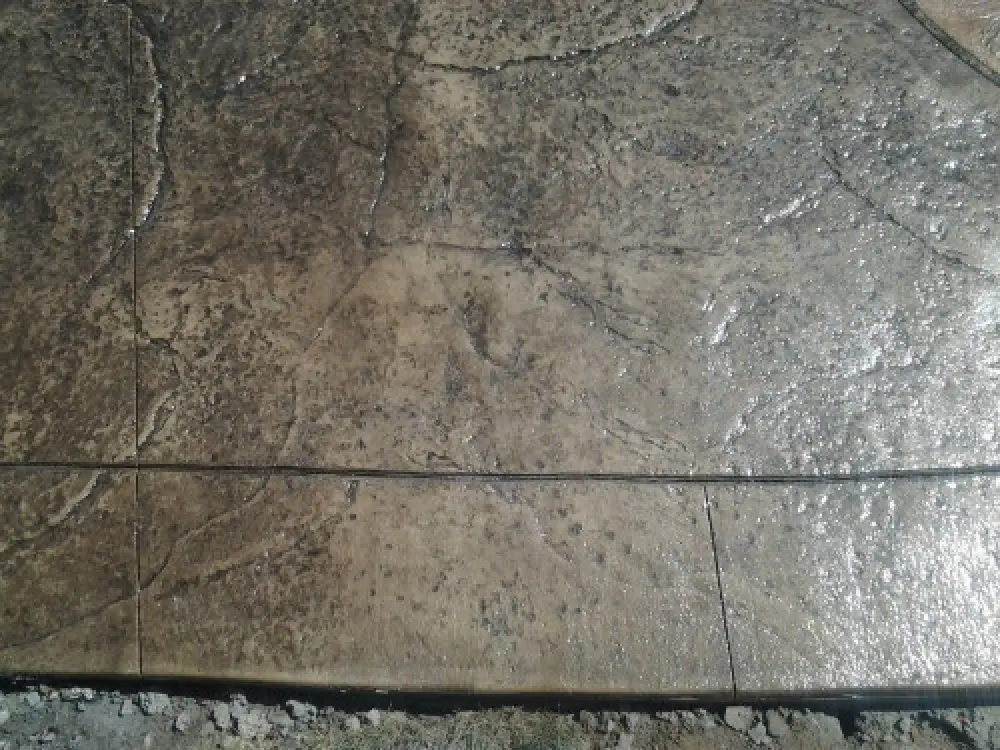 Close-up of a textured, wet concrete surface with grooves and rough lines, bordered by dirt.