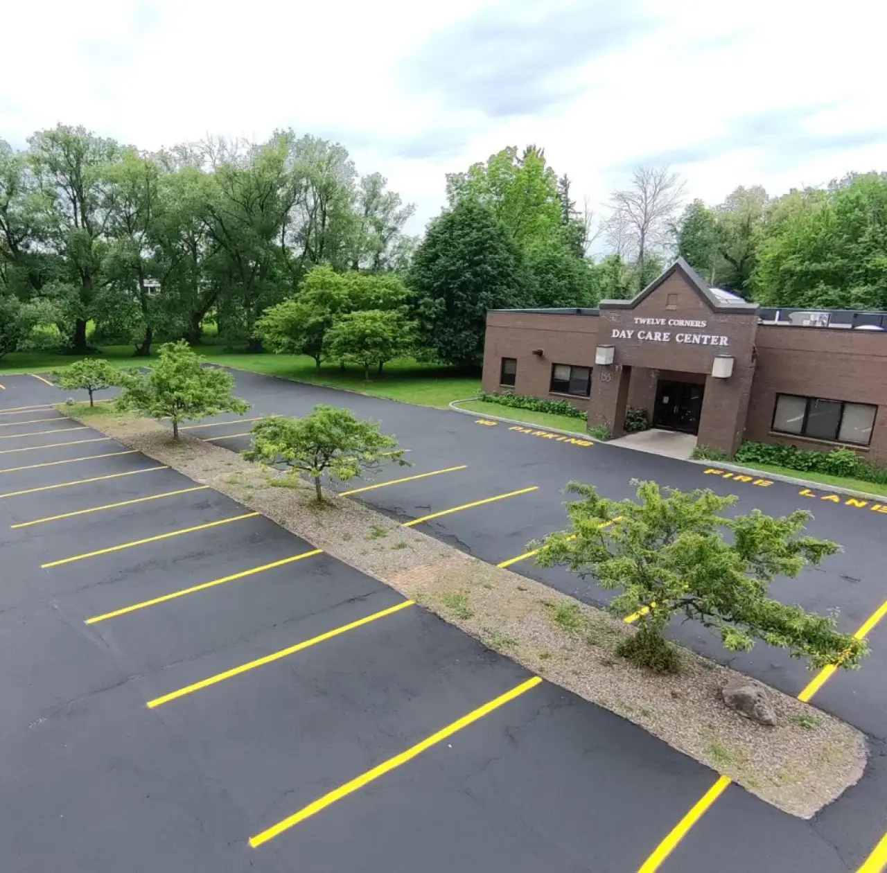 A nearly empty daycare center parking lot with a few trees and marked yellow parking spaces.