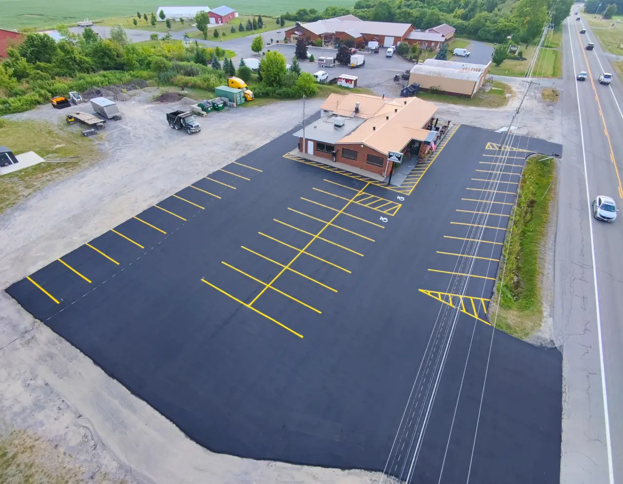 A freshly paved, mostly empty parking lot beside a brick building next to a main road.