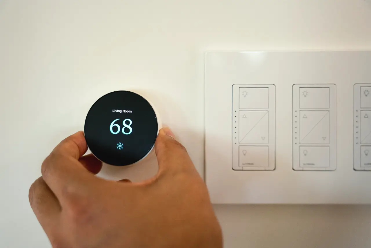 A hand adjusts a smart thermostat set to 68°F next to a panel with three light switches.