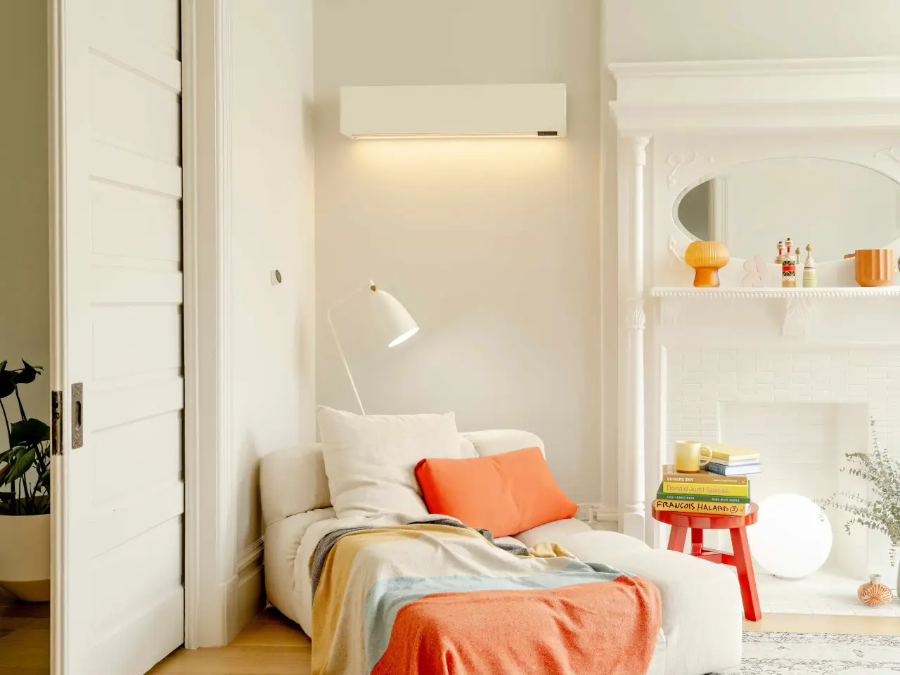 Cozy white sofa with orange pillows, colorful books, and decor near a fireplace and lamp.
