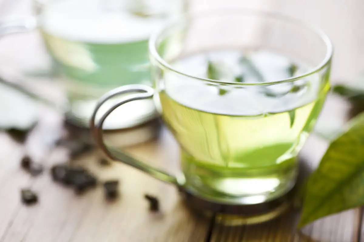 Cup of green tea with loose tea leaves and a fresh leaf.