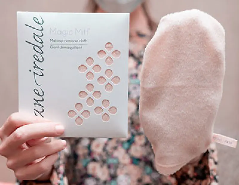 A person holds a package of Magic Mitt makeup remover and a beige cleansing mitt.