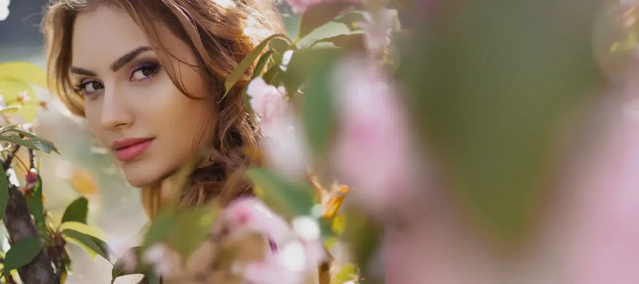 female model looking out from behind pink flower bushes