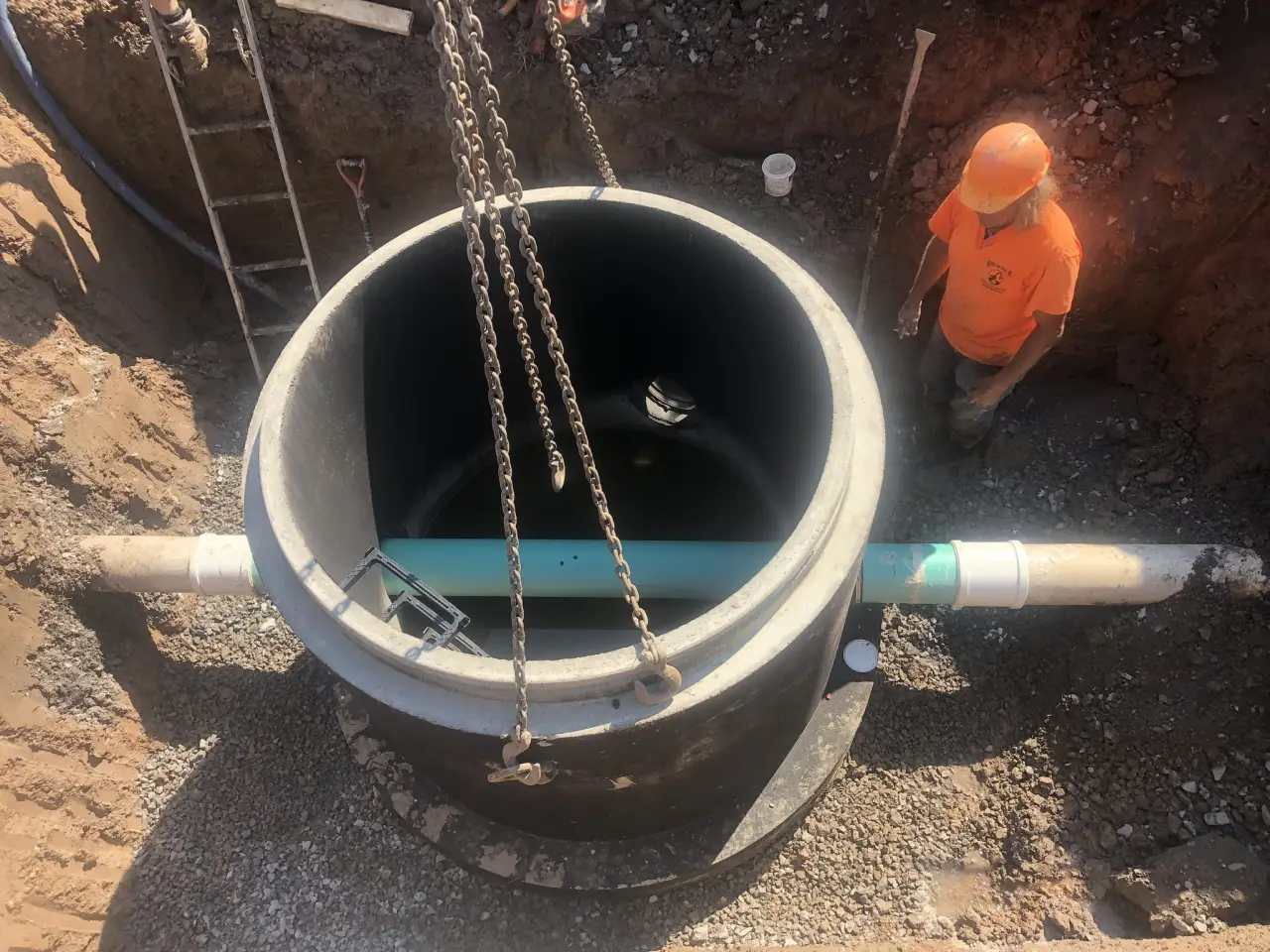 A worker stands beside a large pipe installation at a construction site, viewed from above.