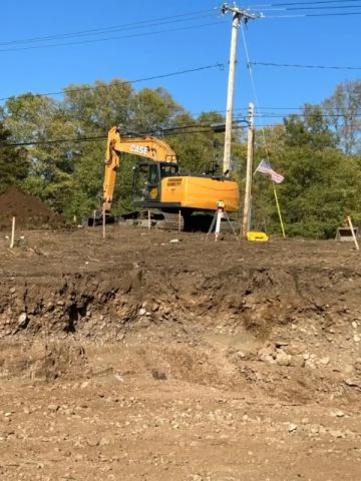 Yellow excavator on a construction site with an American flag and power lines in the background.