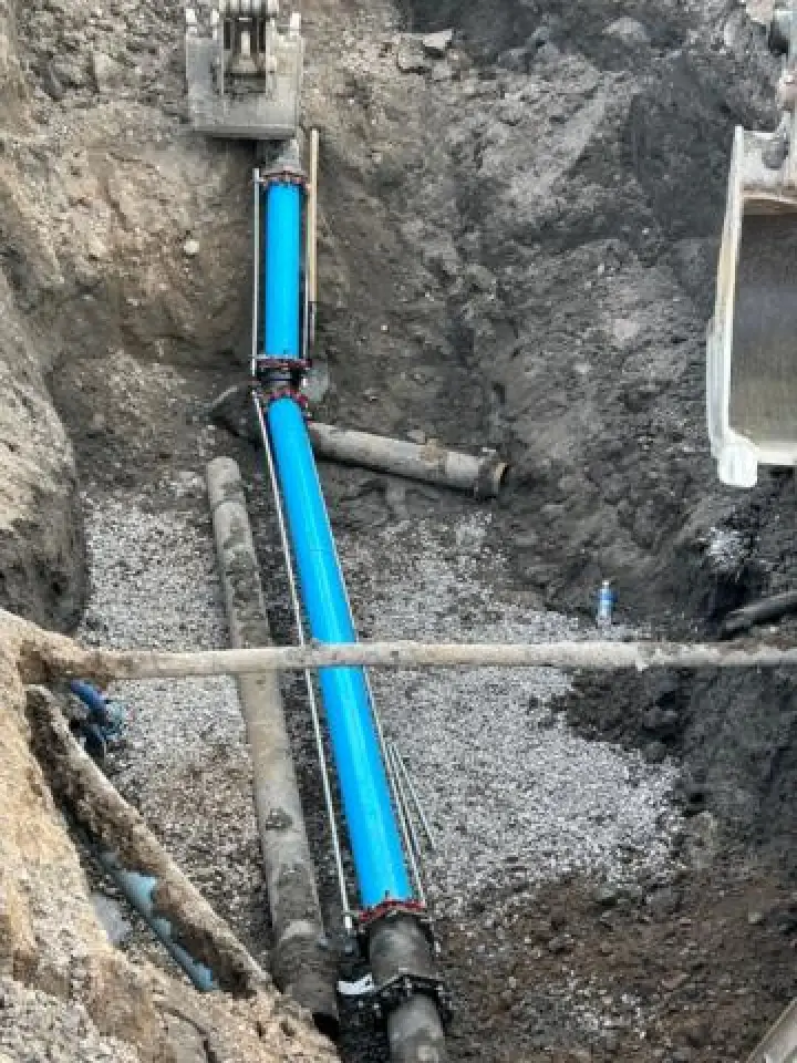 A construction site with a new blue water pipe being installed in a trench.