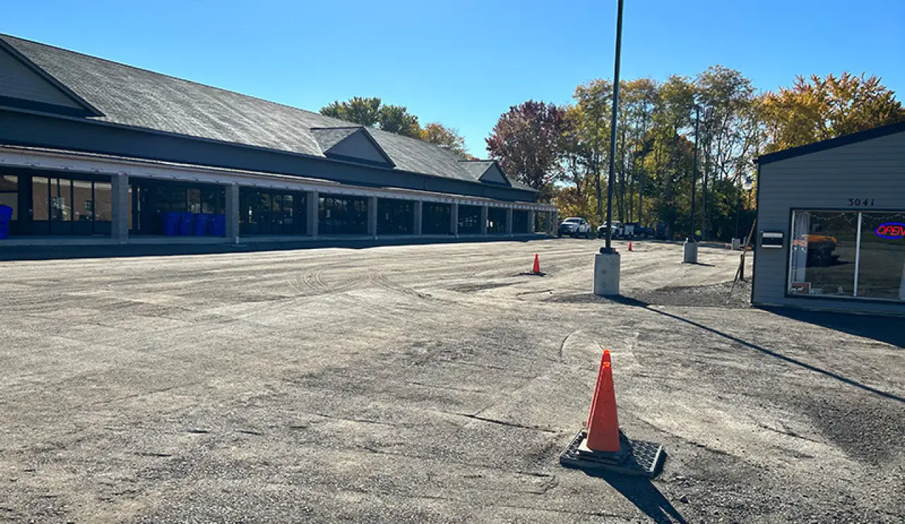 A nearly empty parking lot with orange cones and a building under a clear blue sky.