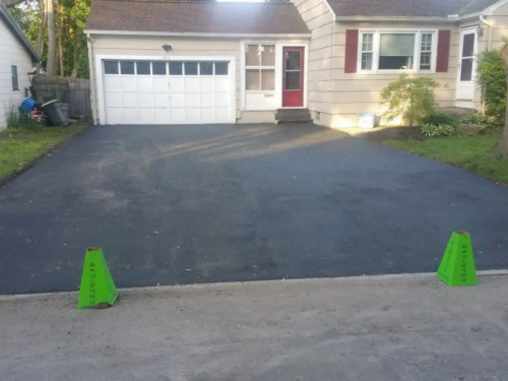 two green cones in front of a freshly paved residential driveway