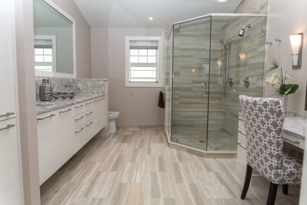 Remodeled bathroom with travertine tile, glass shower, and white vanity.