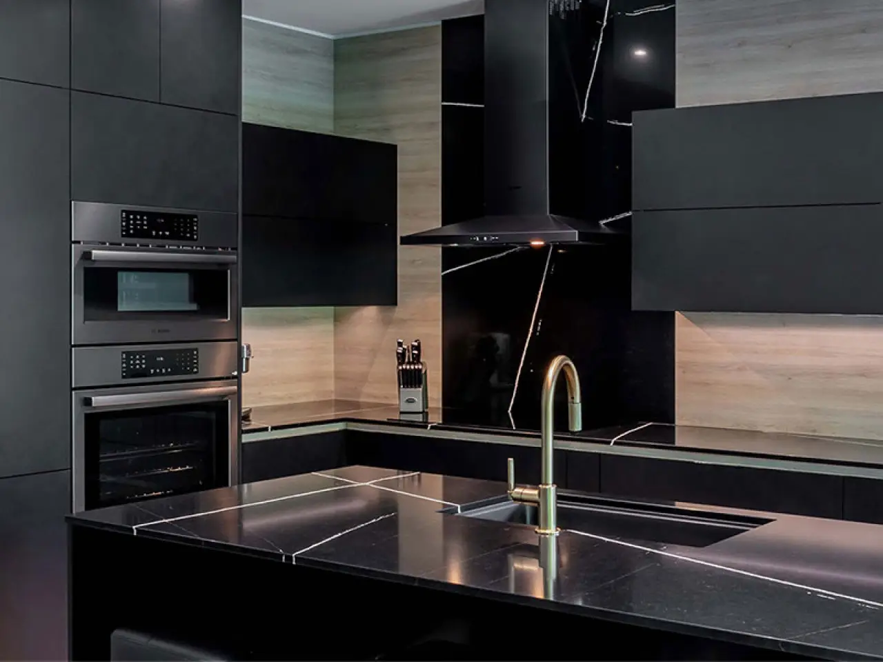 Modern kitchen with black Artcraft cabinetry, marble countertops, a gold faucet, and built-in appliances.