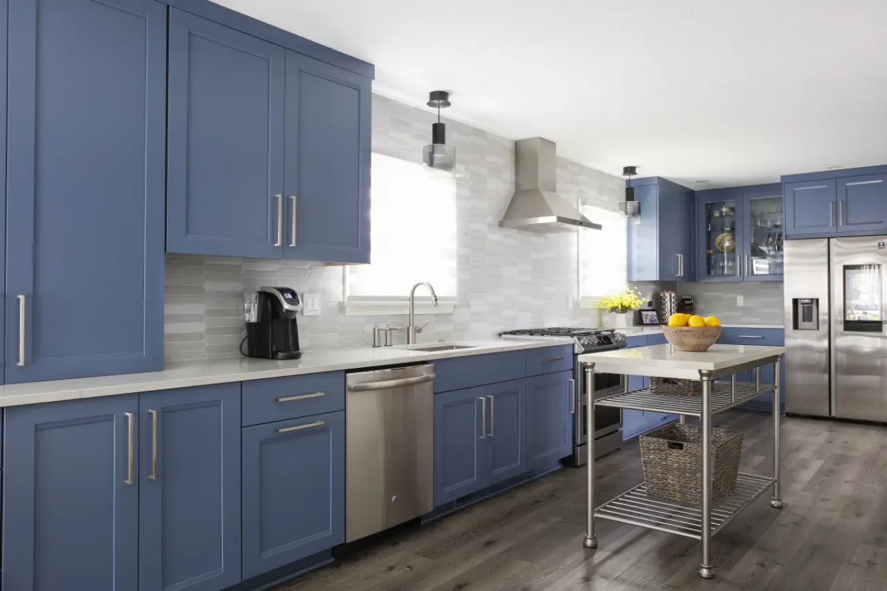 A kitchen with blue cabinets, white countertops and a stainless steel kitchen island on wheels.