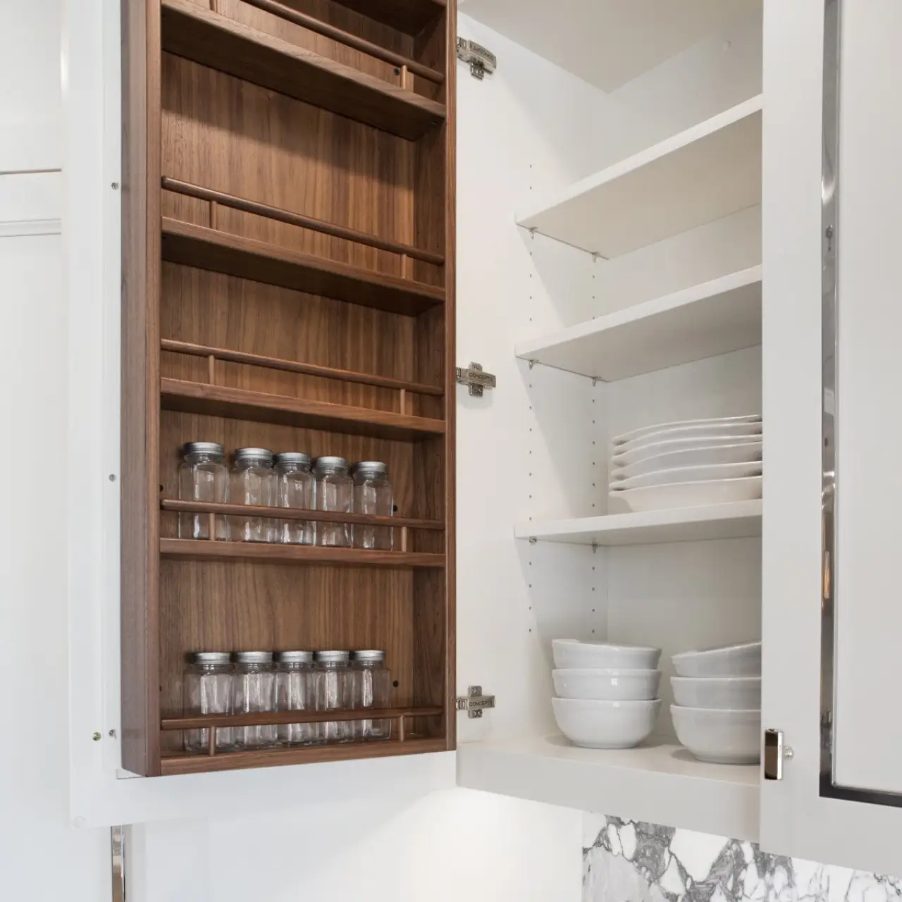 Open kitchen cabinet showing empty wooden spice racks and stacked white dishes on shelves.