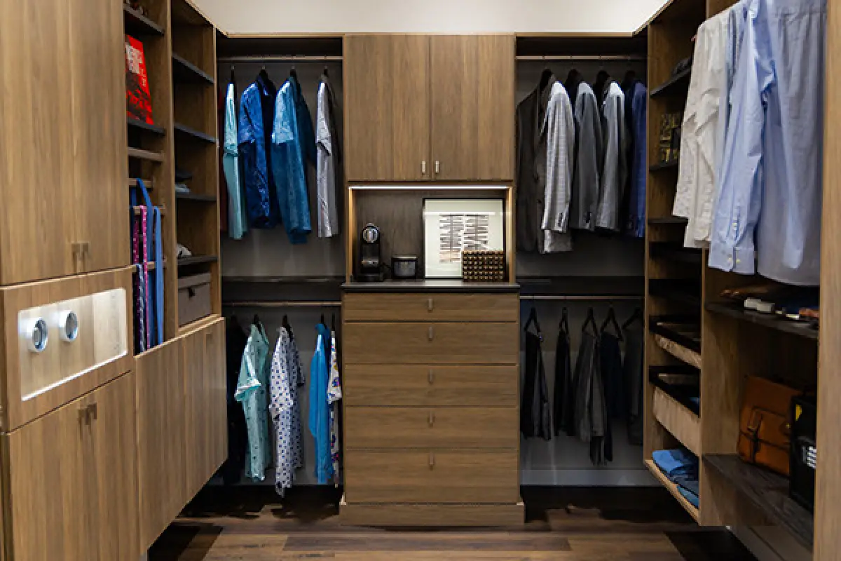 Modern walk-in closet with wooden shelves, hanging shirts, drawers, and accessories organized.