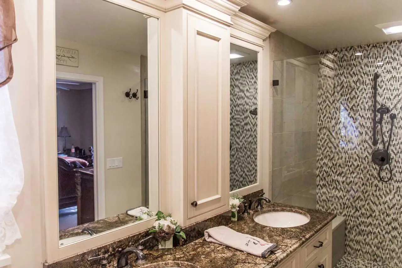Cream double vanity with granite countertop beside a mosaic-tiled walk-in shower.