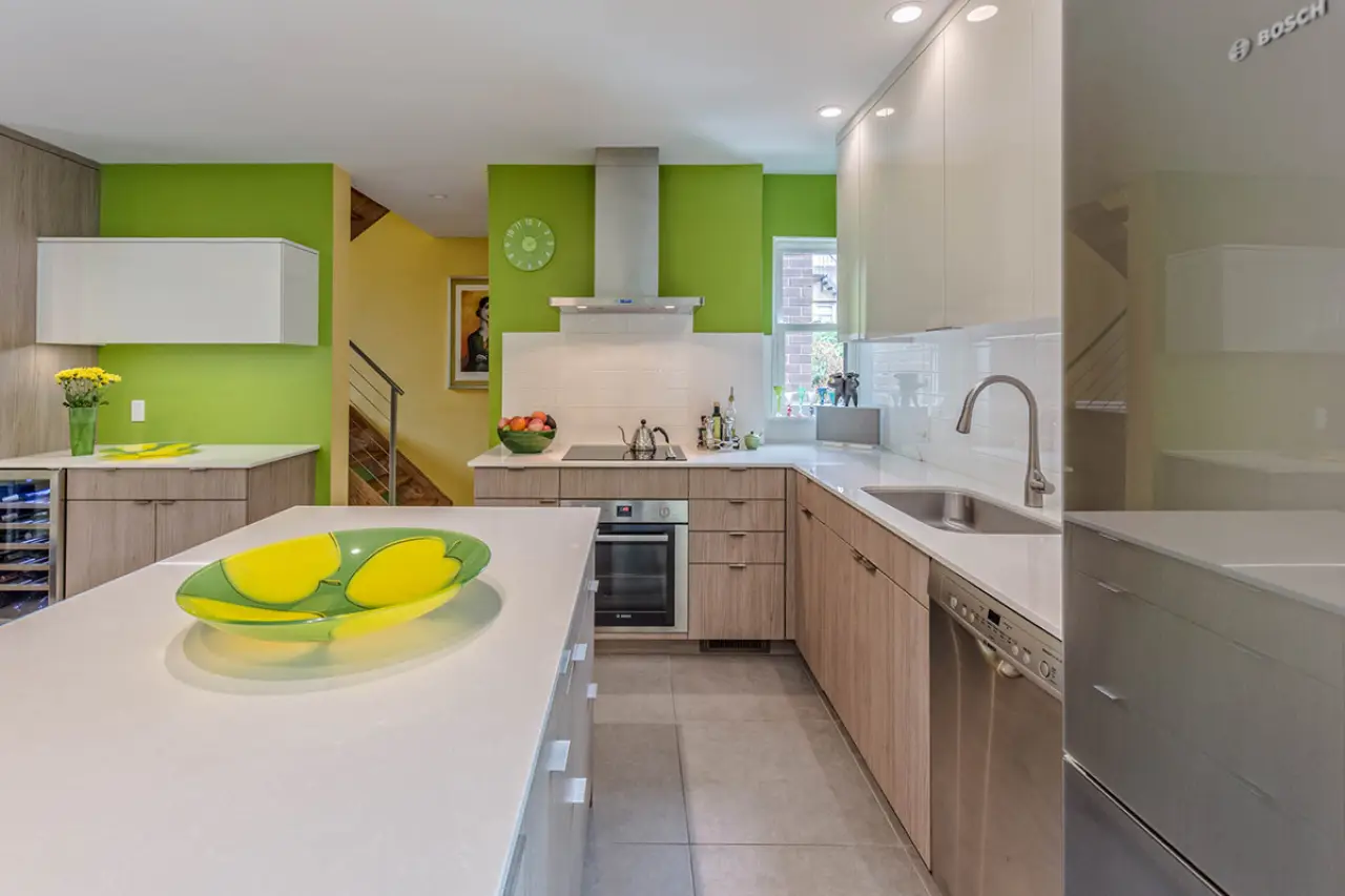 Modern kitchen with green accent walls, wood cabinets, and a white island with a green bowl.