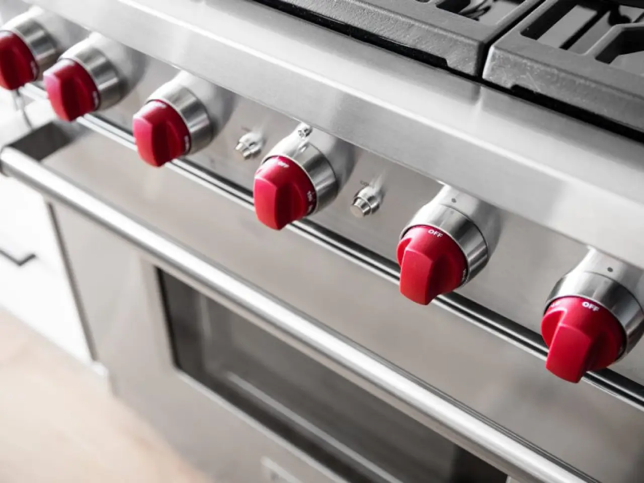 Close-up of a stainless steel oven with five red control knobs above the oven door.