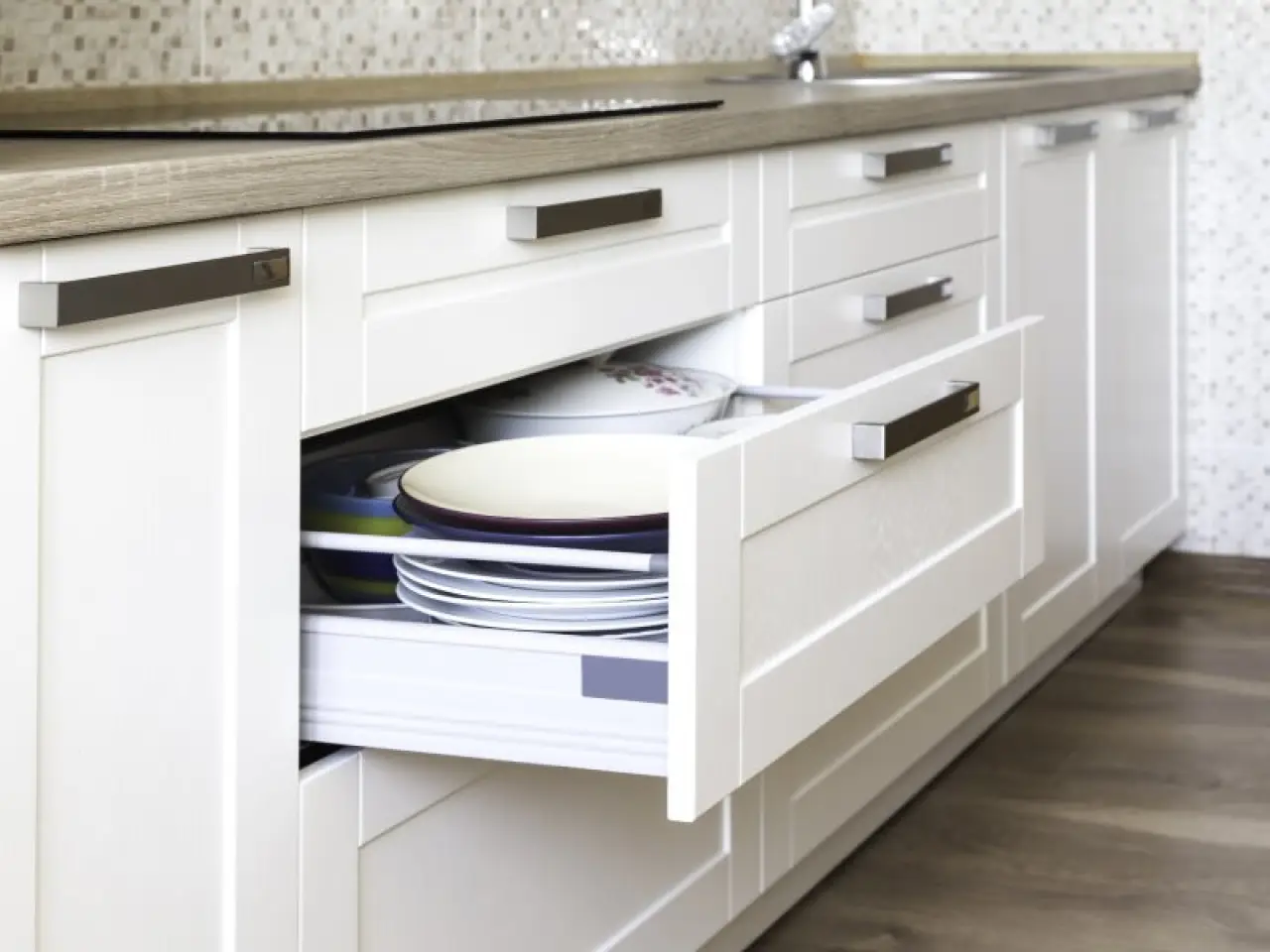 White kitchen cabinets with an open drawer showing stacked plates inside.
