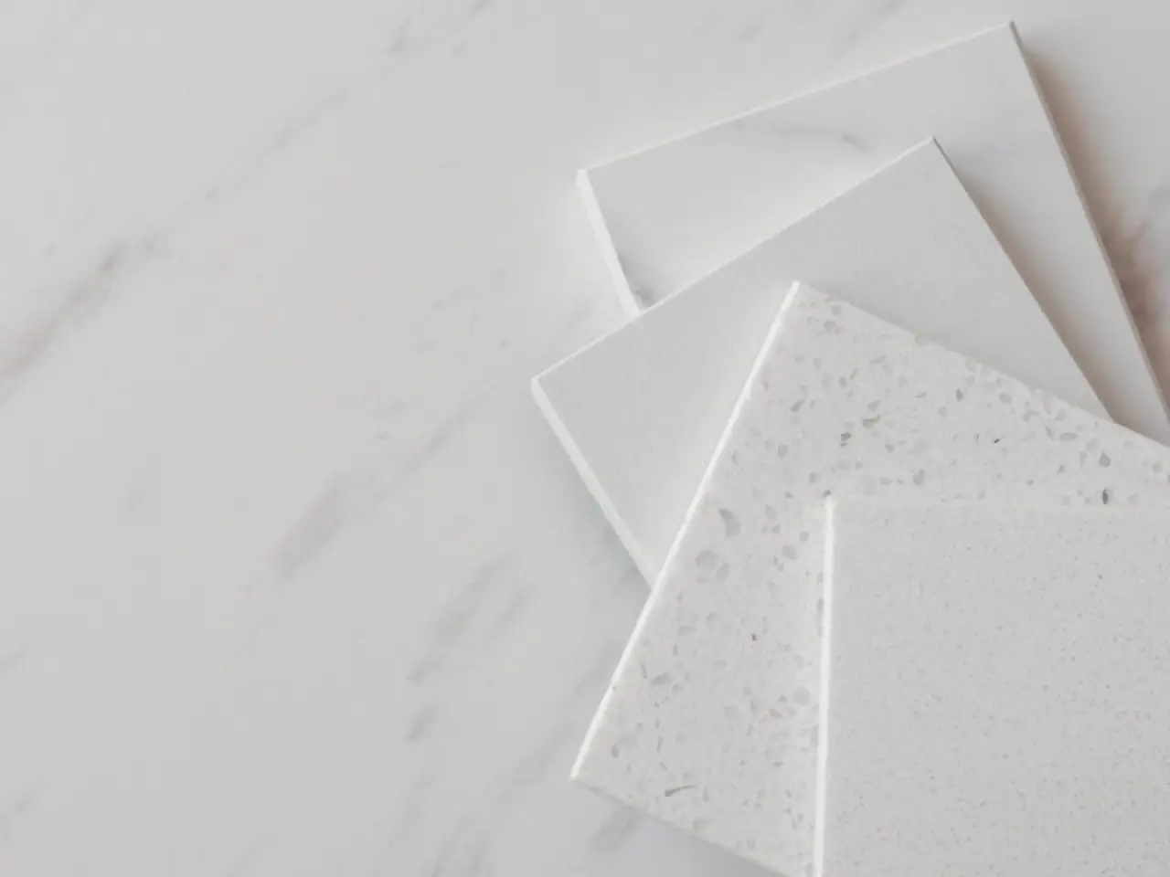 Four white and light gray stone countertop samples arranged on a marble surface.