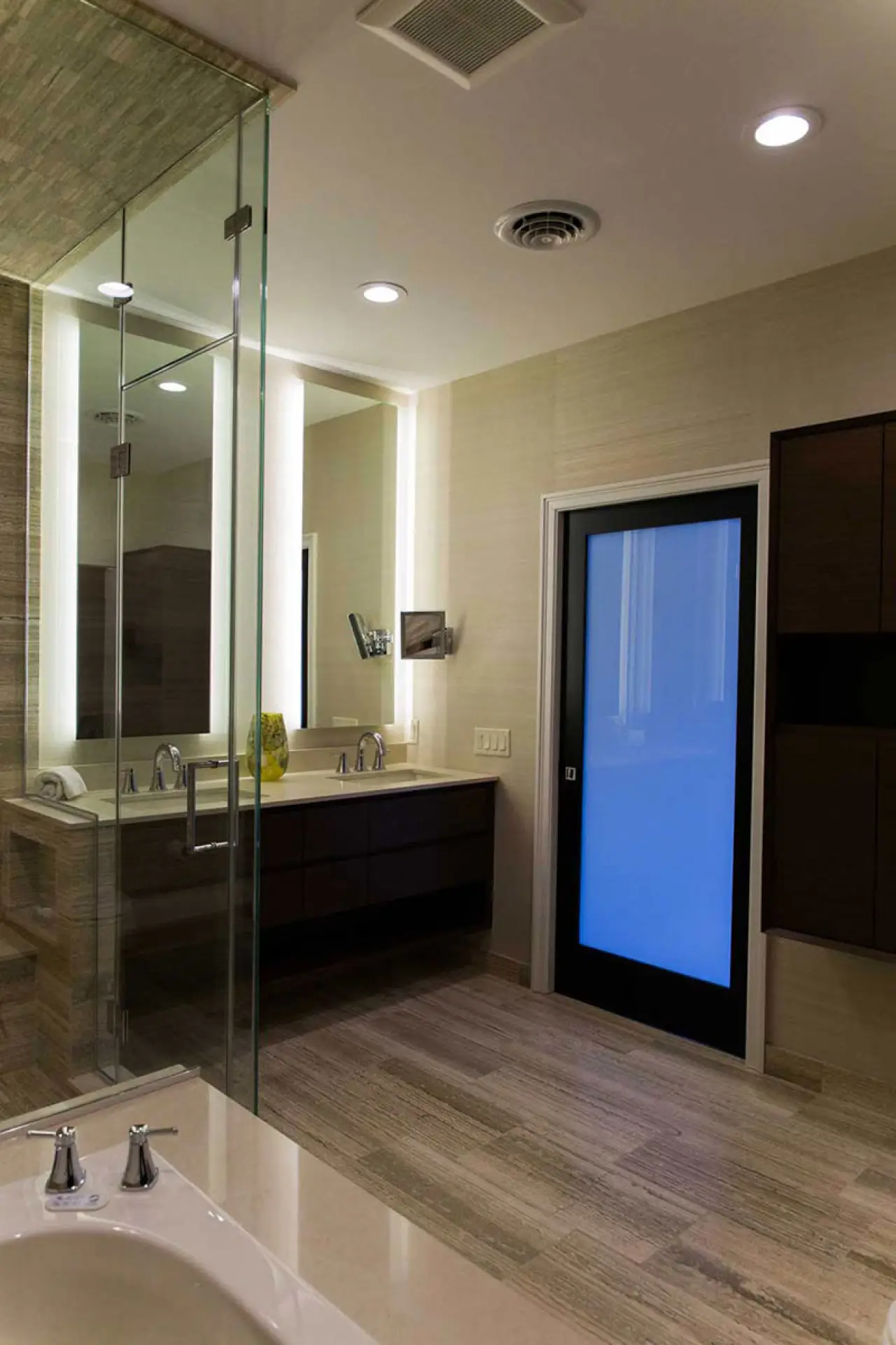 Resort-style bathroom with glass shower, dark wood vanity, and illuminated mirror.