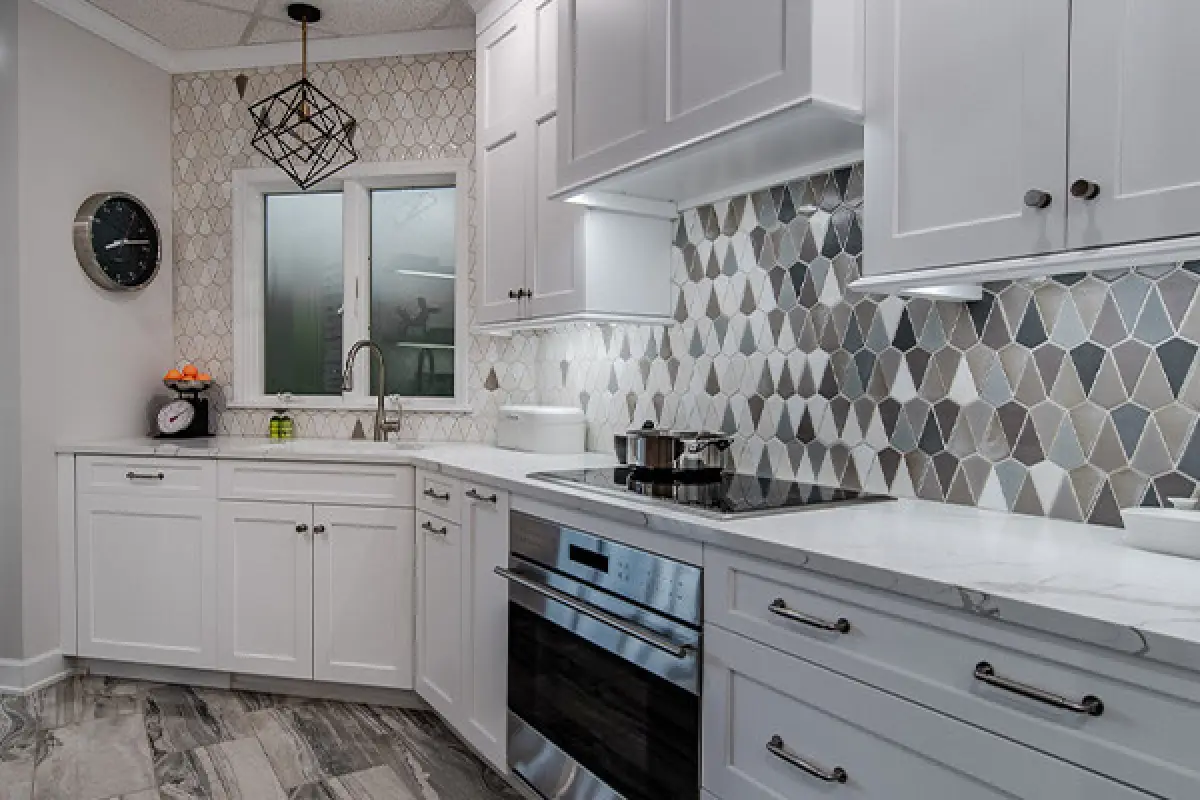 Modern kitchen with white cabinets, geometric tile backsplash, and stainless steel appliances.