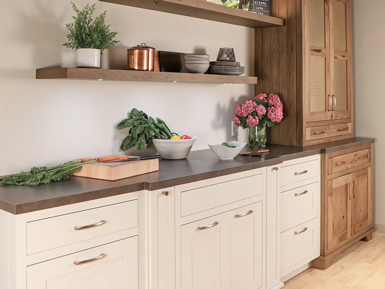 Modern kitchen with white custom cabinetry, wooden shelves, fresh vegetables, and pink flowers.