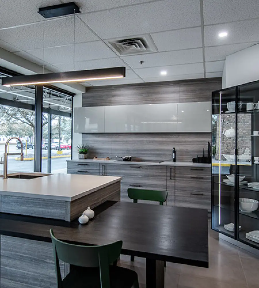 Modern kitchen with gray cabinets, island, dark table, green chairs, and glass display case.