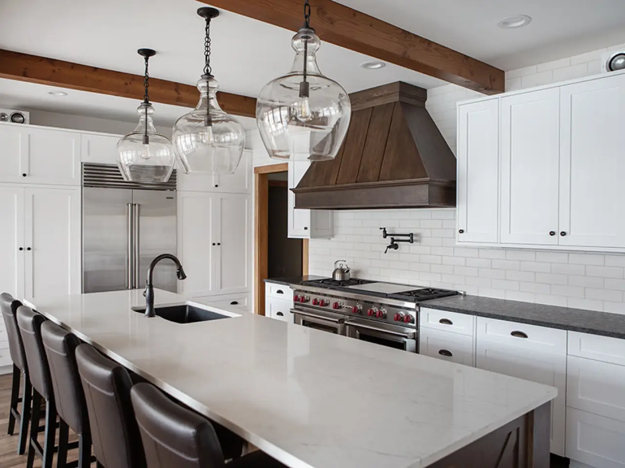 Modern kitchen featuring white Wood-Mode cabinets, a marble island, pendant lights, and dark wood accents.