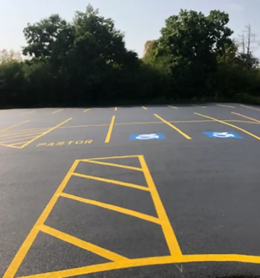 freshly redone parking lot showing a pastor parking spot and two handicapped spots