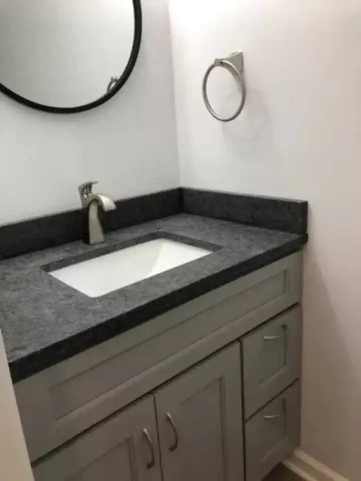 Small bathroom vanity with a gray countertop, sink, faucet, mirror, and towel ring.