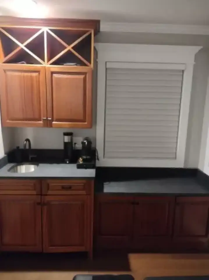 Small kitchen area with dark countertops, wooden cabinets, a sink, and a window with blinds.