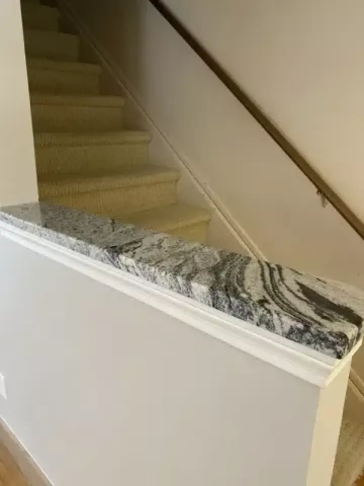 A granite countertop oddly placed on a short wall next to a carpeted staircase.