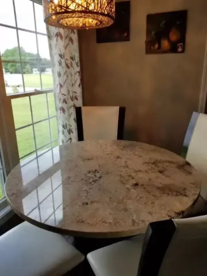 Round marble table with three white chairs near a window, under a decorative hanging light.