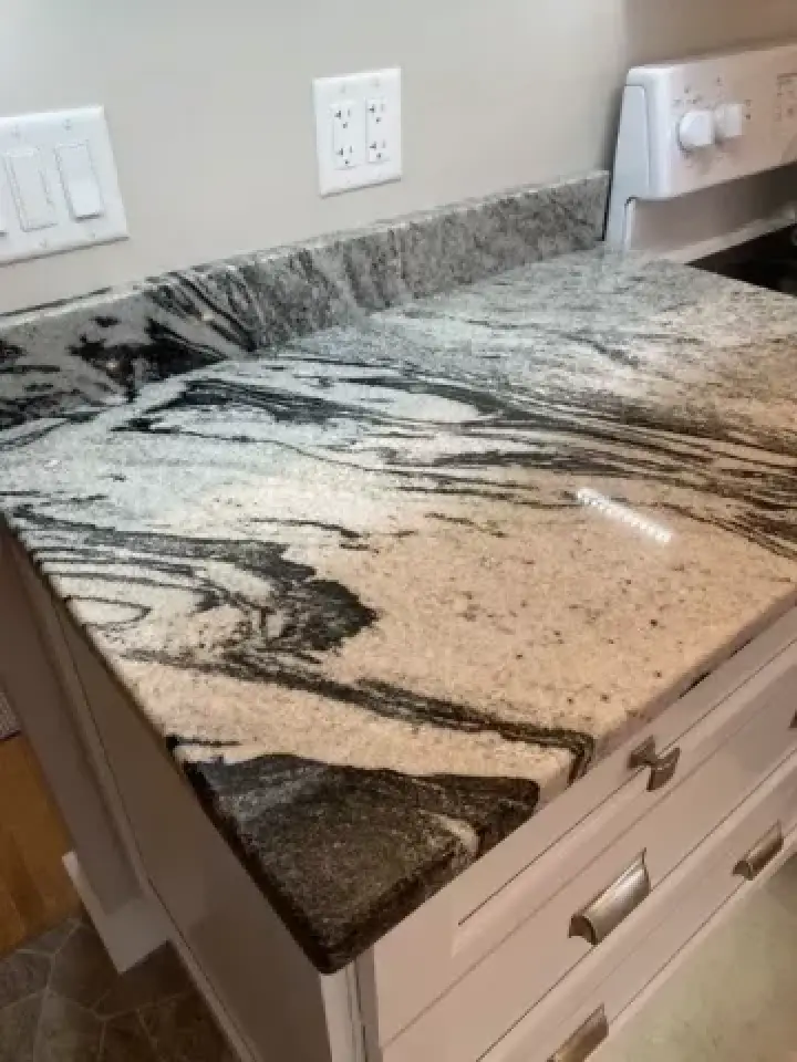 Granite kitchen countertop with black and white swirling patterns, next to a stove and outlets.